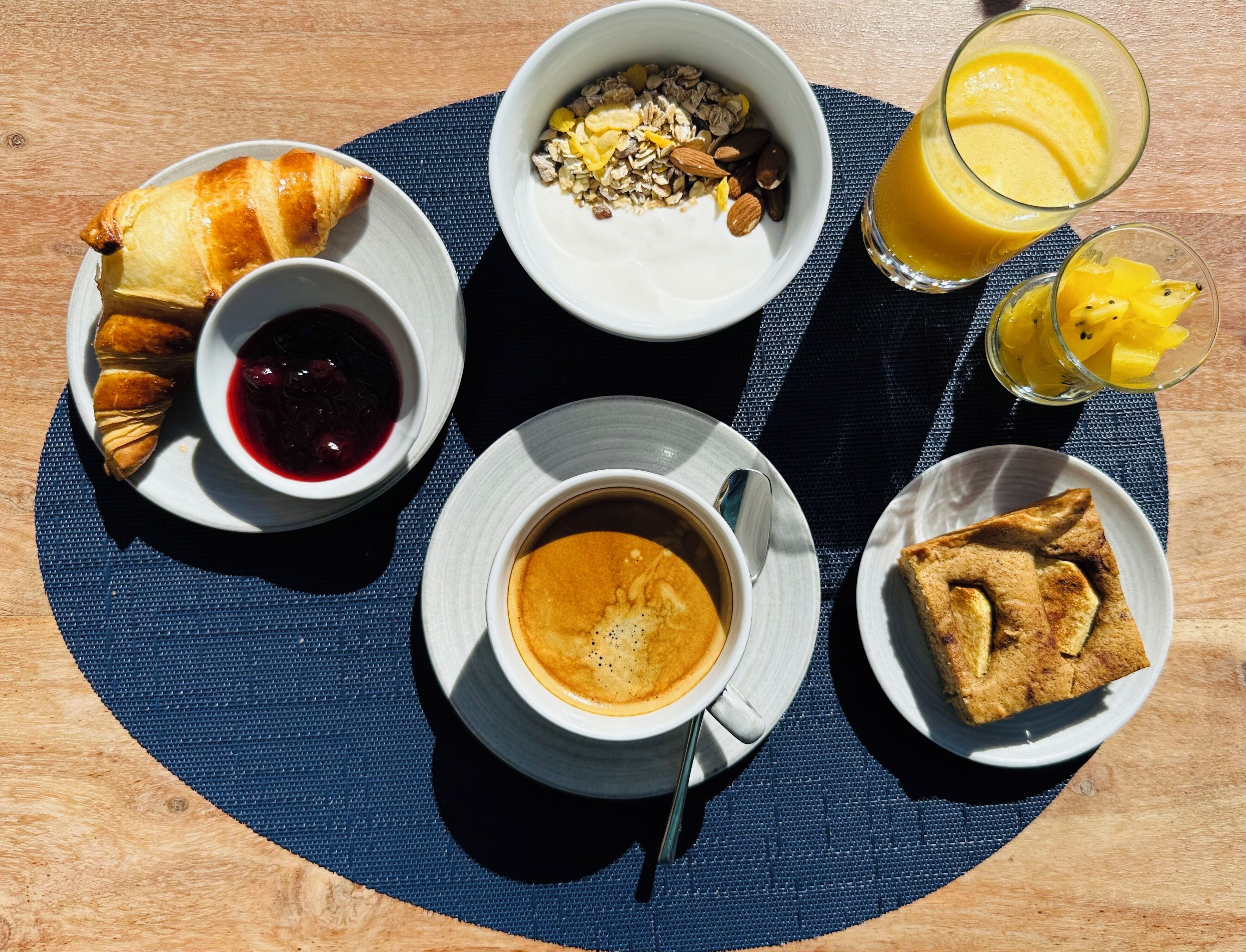 Ein Frühstücksbuffet mit Croissants, Obst, Joghurt, Kaffee und Saft auf einem Tisch.