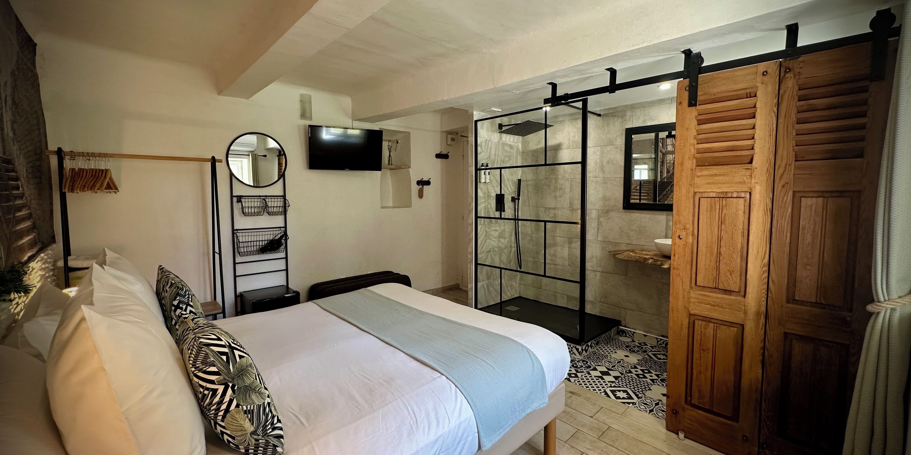 A bedroom with a bed, a TV, a shower area, and a wooden door.