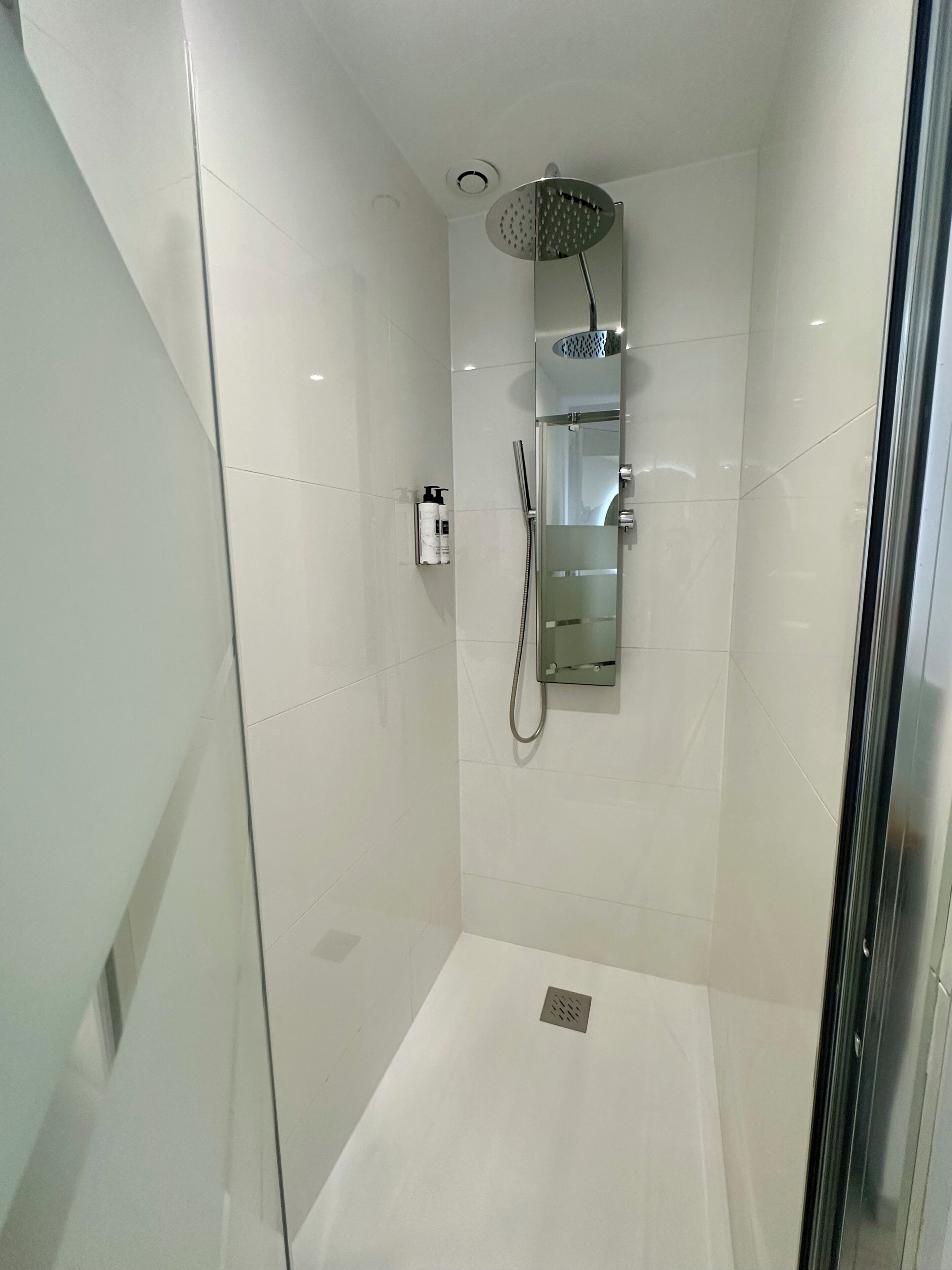 A modern shower with a handheld showerhead, a glass-enclosed shower area, and a small shelf with toiletries.