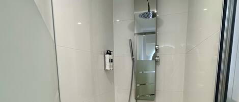 A modern shower with a handheld showerhead, a glass-enclosed shower area, and a small shelf with toiletries.