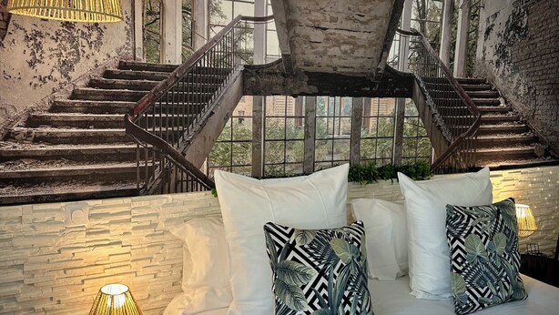 Une chambre à coucher comprenant un lit, des oreillers, une table de chevet, une lampe et un escalier menant à un espace extérieur.