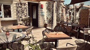Un espace extérieur aménagé en terrasse, avec des tables et des chaises, une plateforme en bois et un bâtiment sur lequel est apposée une enseigne indiquant « HÔTEL Le CLOS du DRAMONT ».