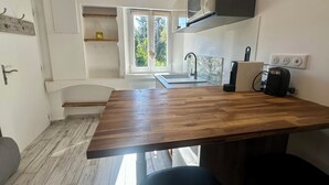 Une cuisine moderne dotée d’un plan de travail en bois, d’un four à micro-ondes encastré, d’un évier avec un pare-éclaboussures en verre et d’une fenêtre donnant sur un espace verdoyant.