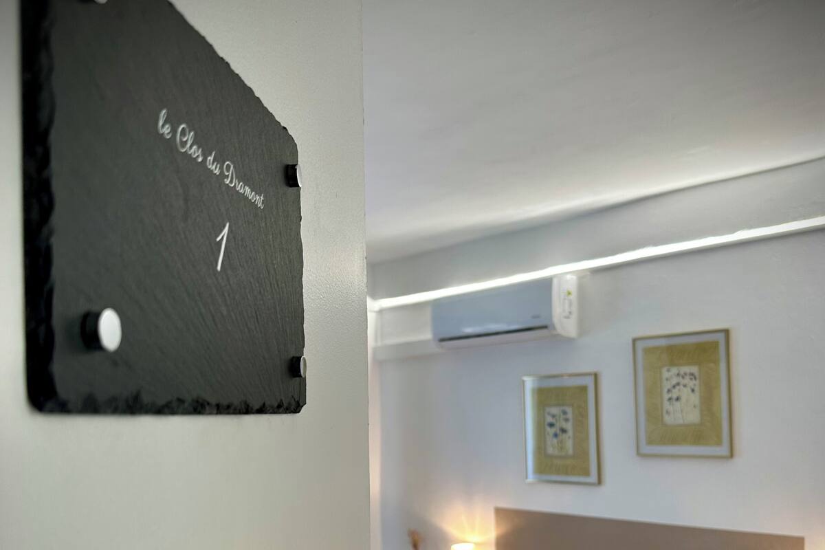 A bedroom with a bed, a bedside table, a wall-mounted air conditioner, and framed pictures.