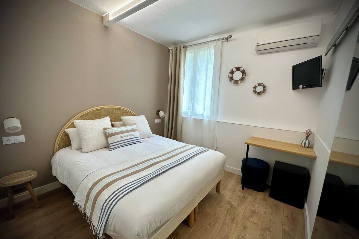 A bedroom with a bed, bedside table, wall-mounted TV, and an air conditioning unit.