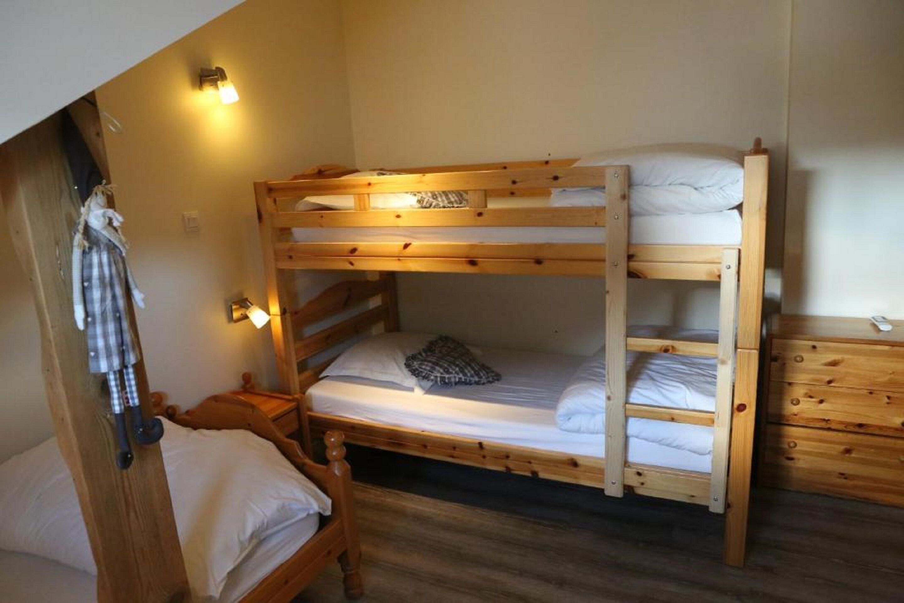 Ein Schlafraum mit Etagenbetten, Holzboden, Nachttisch und Kommode.