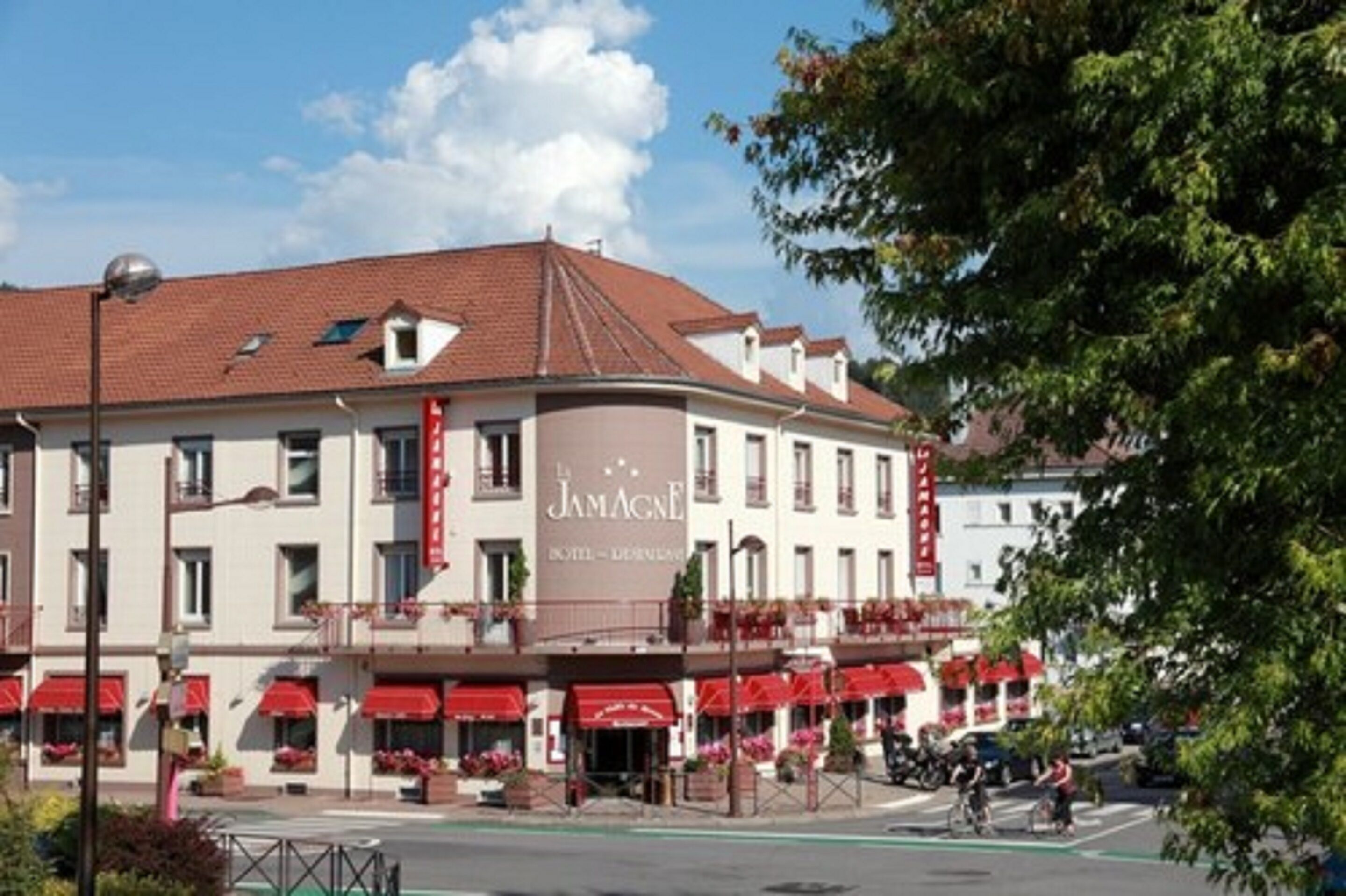 Un hotel con fachada curva, toldos rojos y un cartel que dice "La Jamagne Hotel - Les Bains".