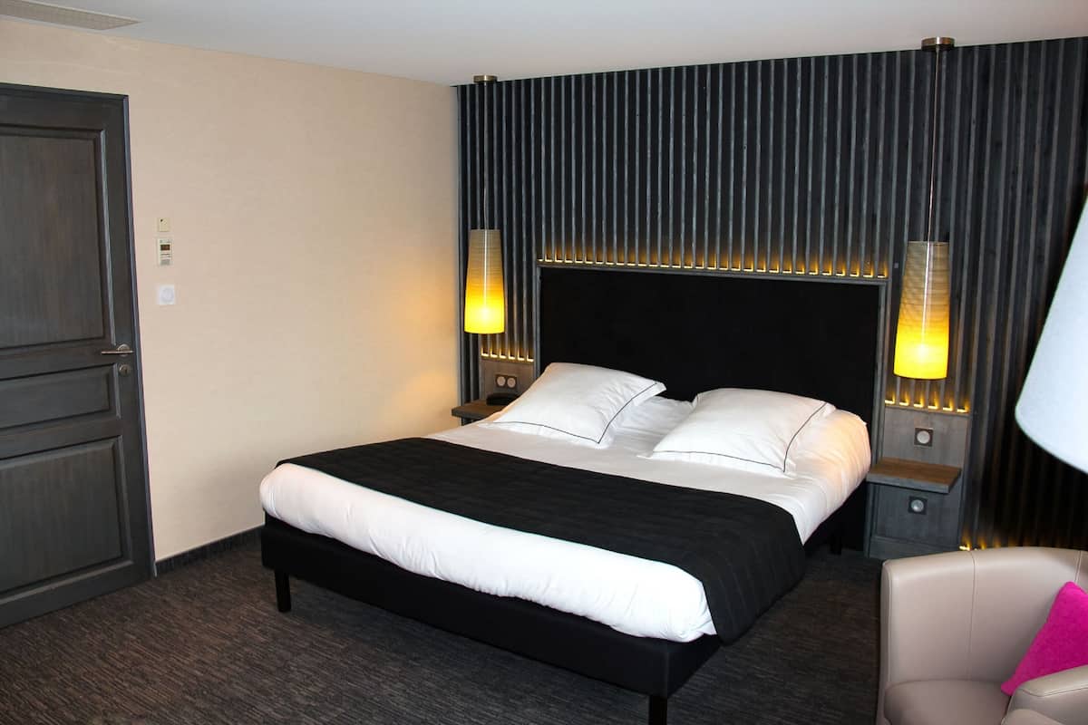Una habitación de hotel con una cama grande, dos lámparas de noche, una mesita de noche y una silla.