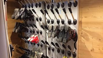 Een wandrek met verschillende ski-laarzen en ski-stokken.