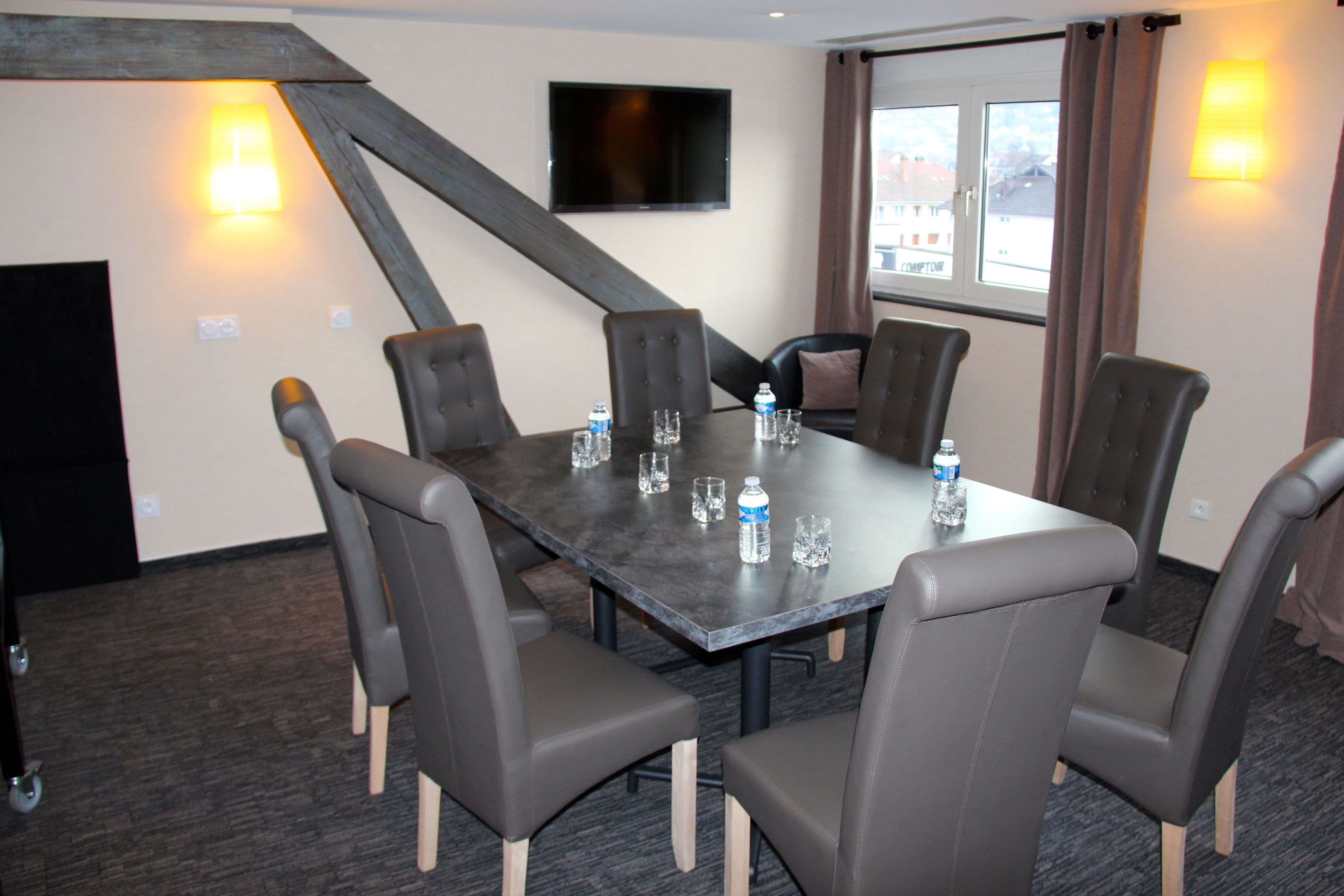 A conference room with a dark table, six chairs, a flat-screen TV, and two wall-mounted lamps.