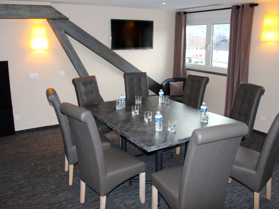 A conference room with a dark table, six chairs, a flat-screen TV, and two wall-mounted lamps.