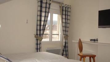 A bedroom with a bed, a chair, a window with curtains, an air conditioning unit, and a wall-mounted television.
