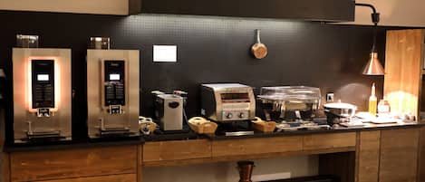 Una cocina con dos máquinas de espresso, un molinillo de café, un hervidor y varios utensilios de cocina sobre la encimera.