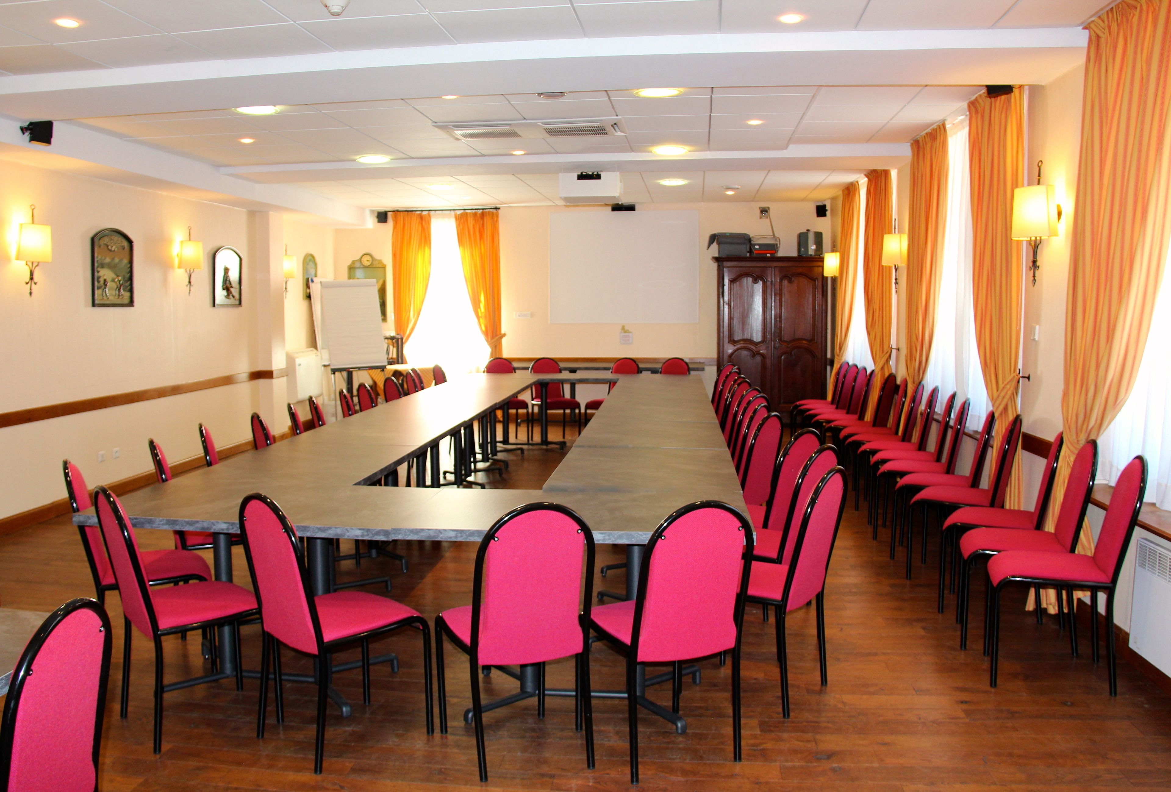 A conference room with a long table and rows of chairs, equipped with a projector and a whiteboard.