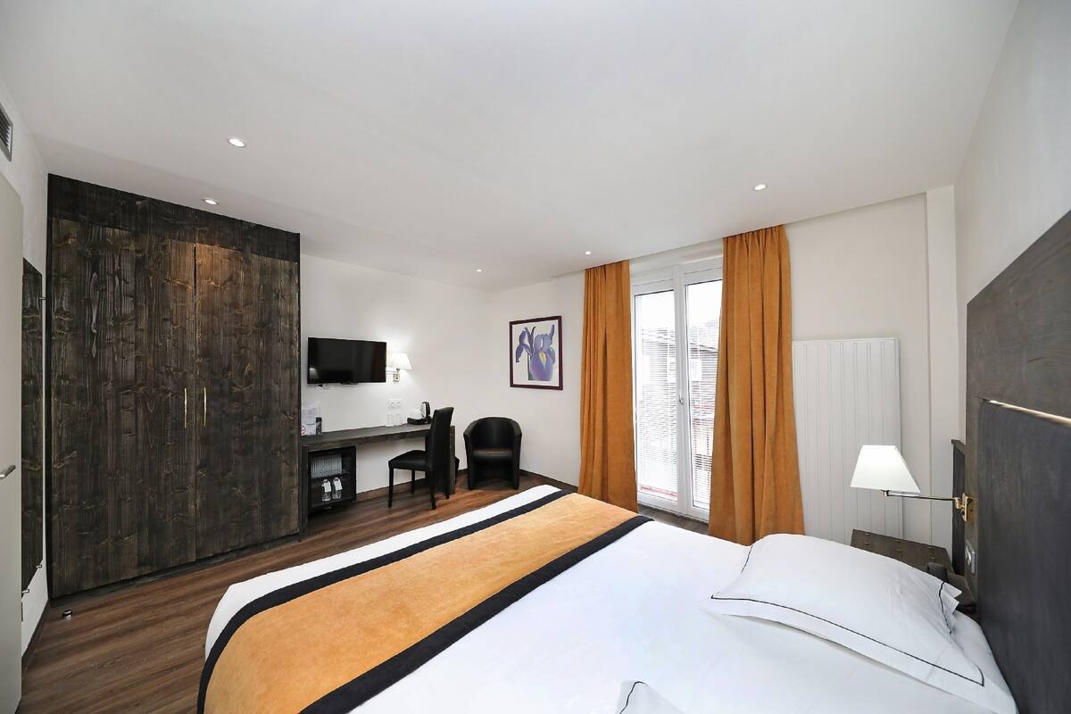 Una habitación de hotel con una cama grande, un escritorio con silla, televisión y ventana con cortinas.