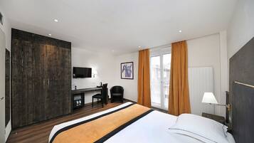 A hotel room with a large bed, a desk with a chair, a television, and a window with curtains.