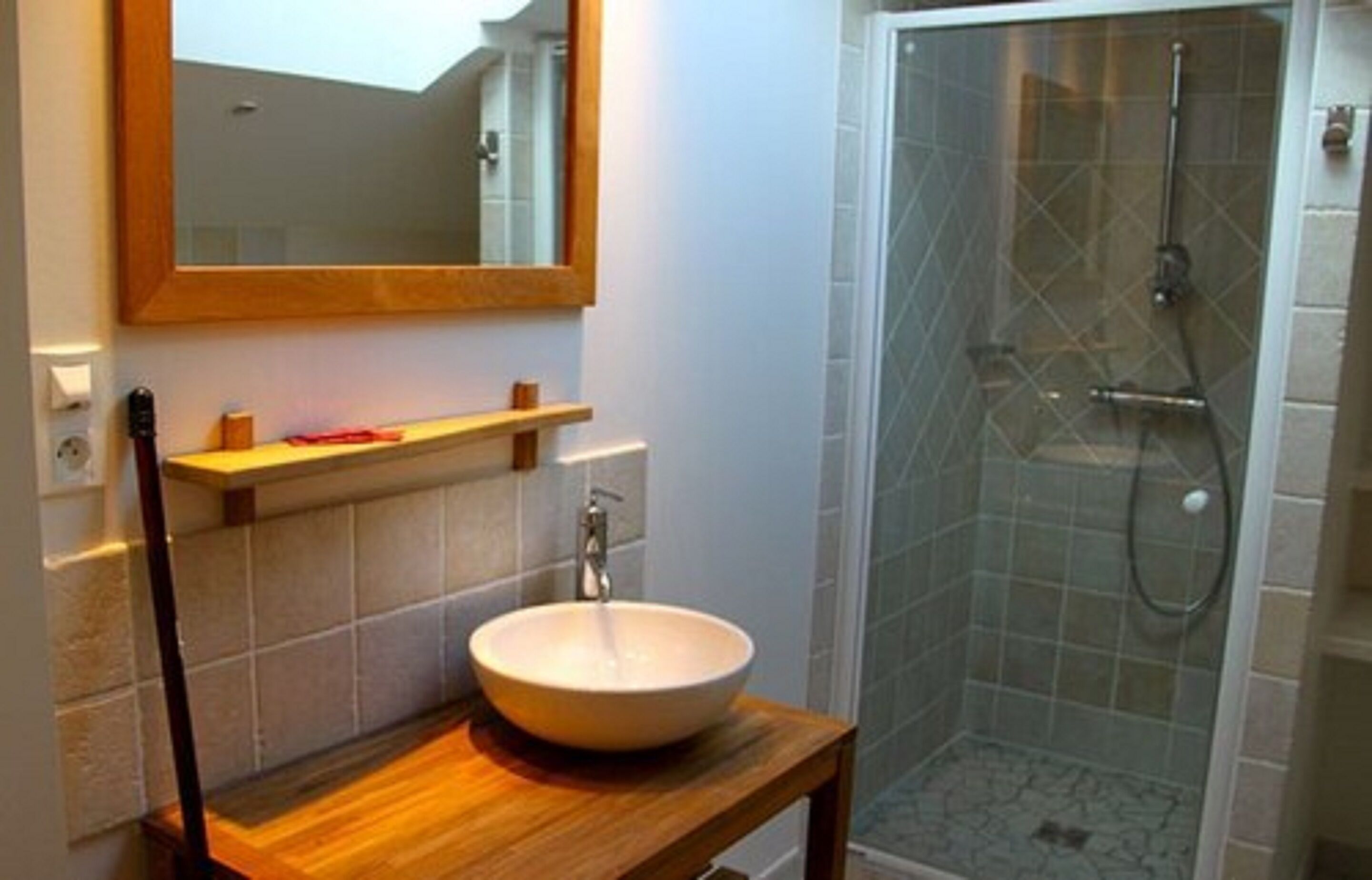 Un baño con tocador de madera, lavamanos blanco y ducha con cerramiento de vidrio.