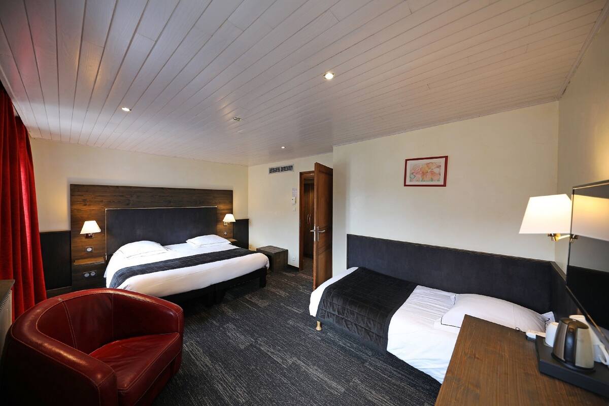 Una habitación de hotel con dos camas, un sillón de cuero rojo, una mesita de noche de madera y un escritorio con lámpara.