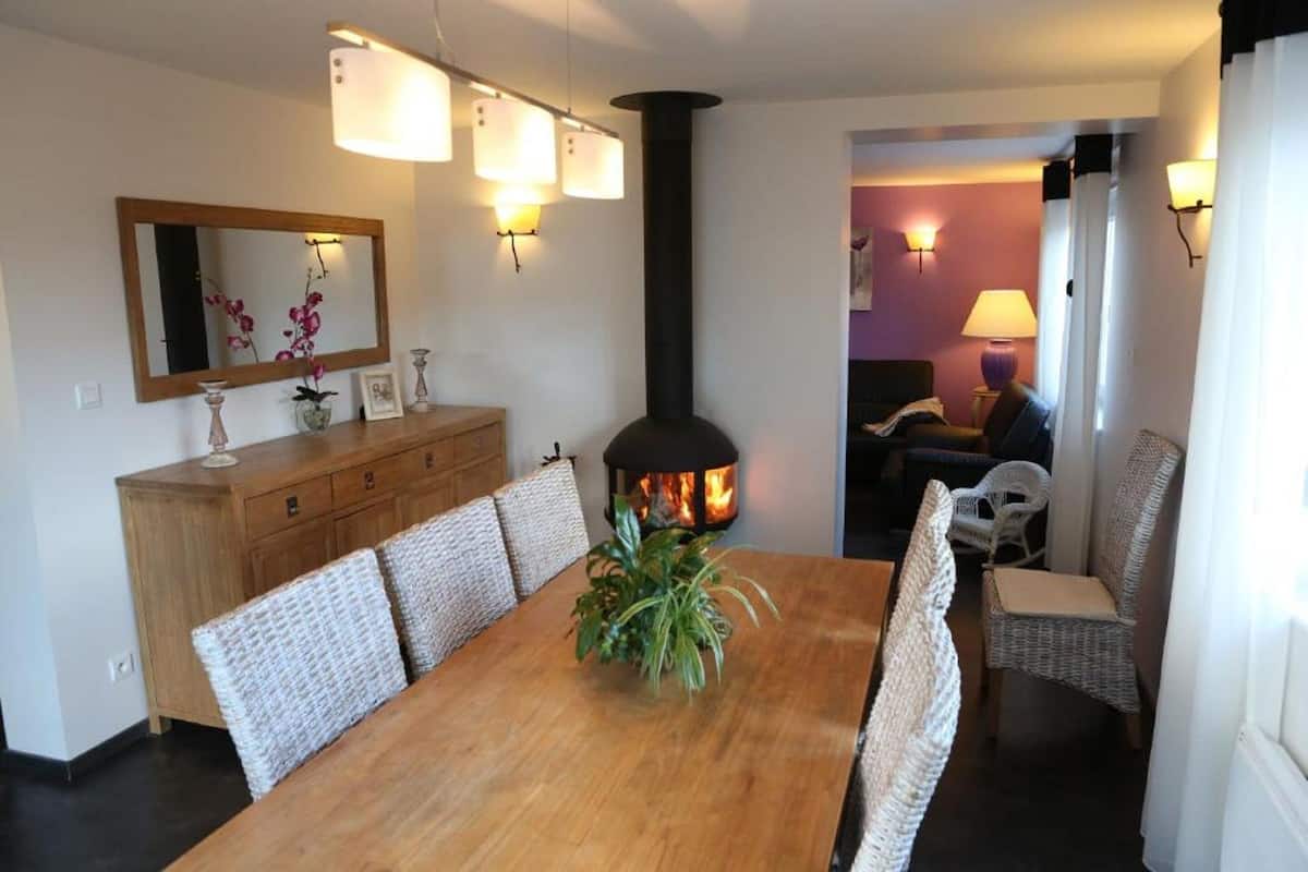 Un comedor con mesa de madera, sillas de mimbre, un espejo y chimenea.
