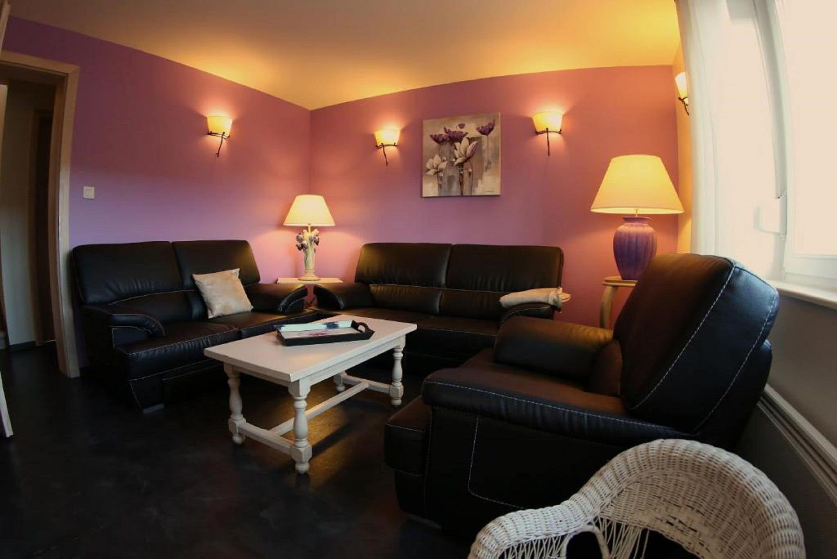 A living room with dark leather sofas, a white coffee table, and two wall-mounted lamps.