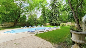Una piscina con sillas de descanso, rodeada de césped cuidado y árboles.