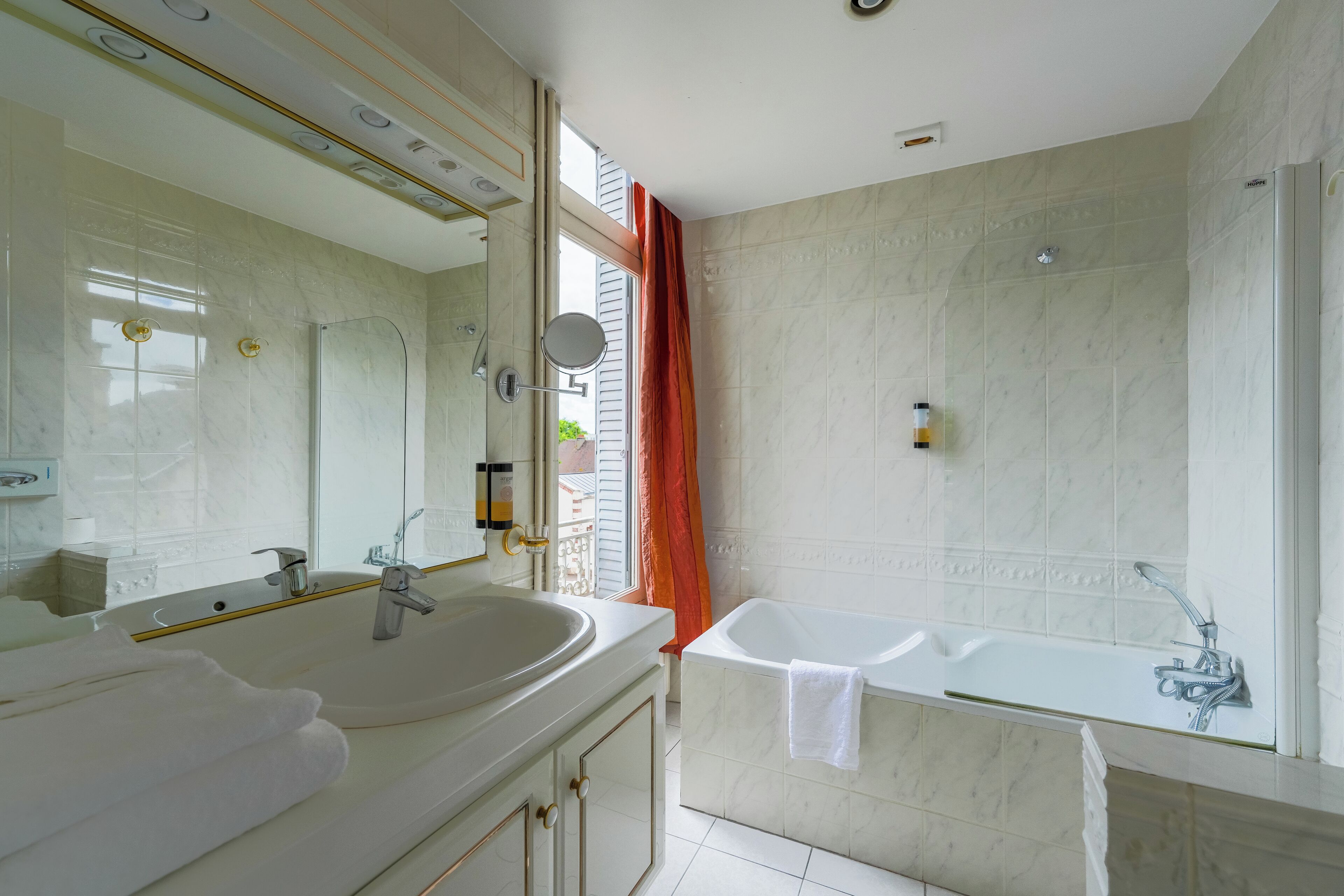 A modern bathroom with a large mirror, dual sinks, a bathtub, and a shower.