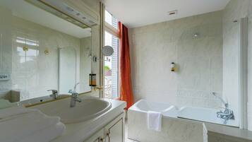 A modern bathroom with a large mirror, dual sinks, a bathtub, and a shower.