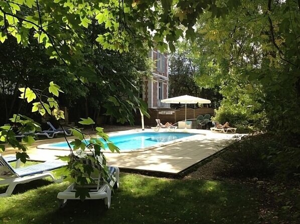 Un patio trasero con piscina, sillas de descanso y una sombrilla.