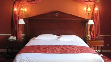 Habitación de hotel con una cama grande, un banco, dos mesitas de noche con lámparas y una cama con dosel y cortinas.
