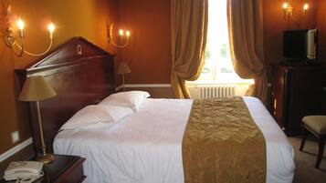 A hotel room with a bed, a desk with a telephone, a lamp, a chair, and a television.