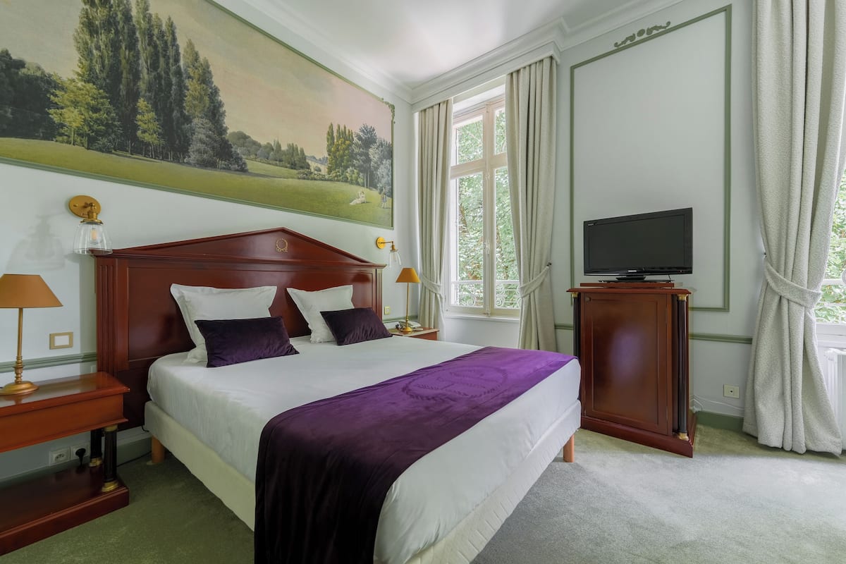 Een hotelkamer met een groot bed, een televisie, een schilderij aan de muur en een raam met gordijnen.