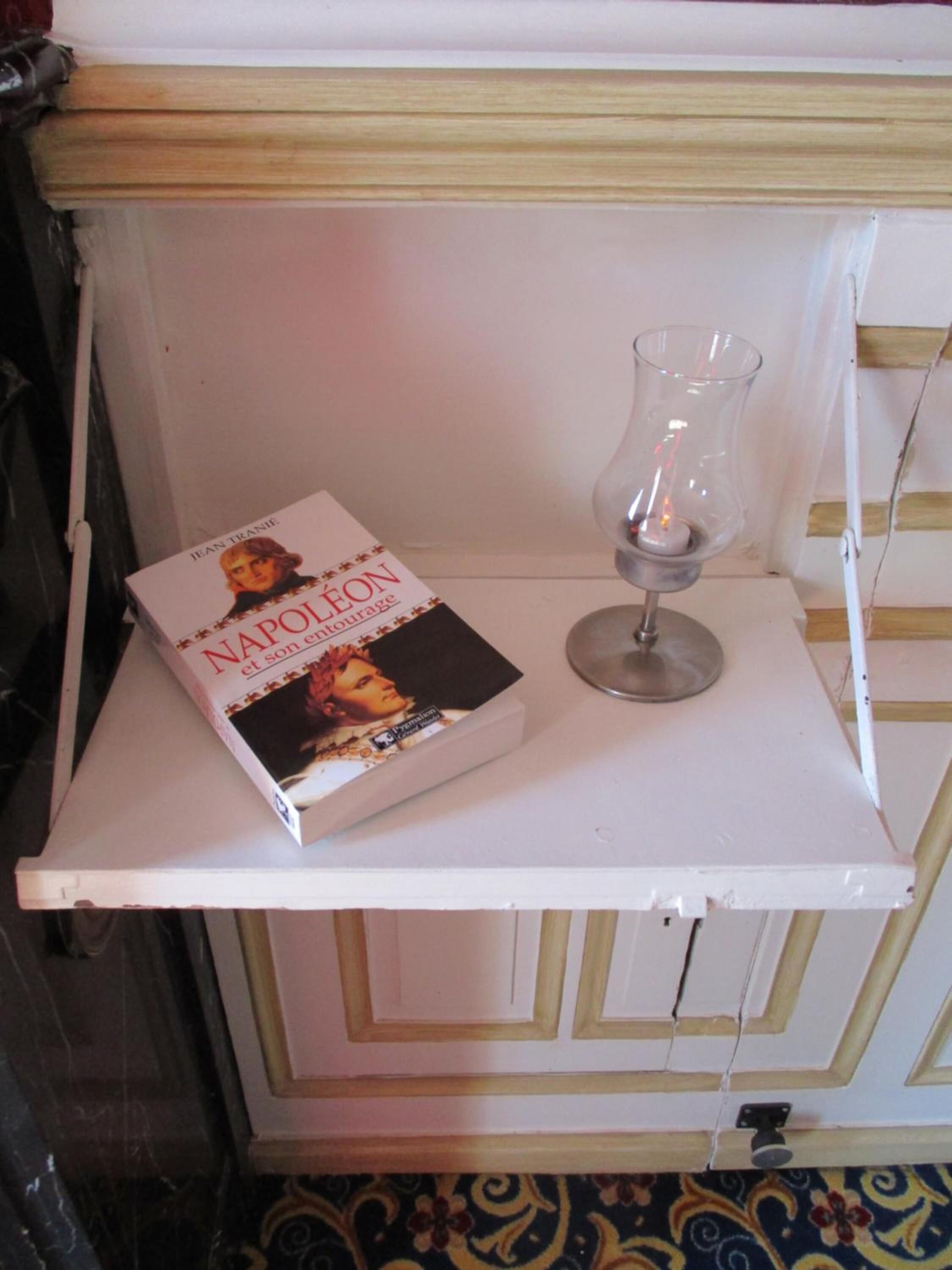 Un livre intitulé « NAPOLÉON » et un verre transparent sur une étagère blanche.