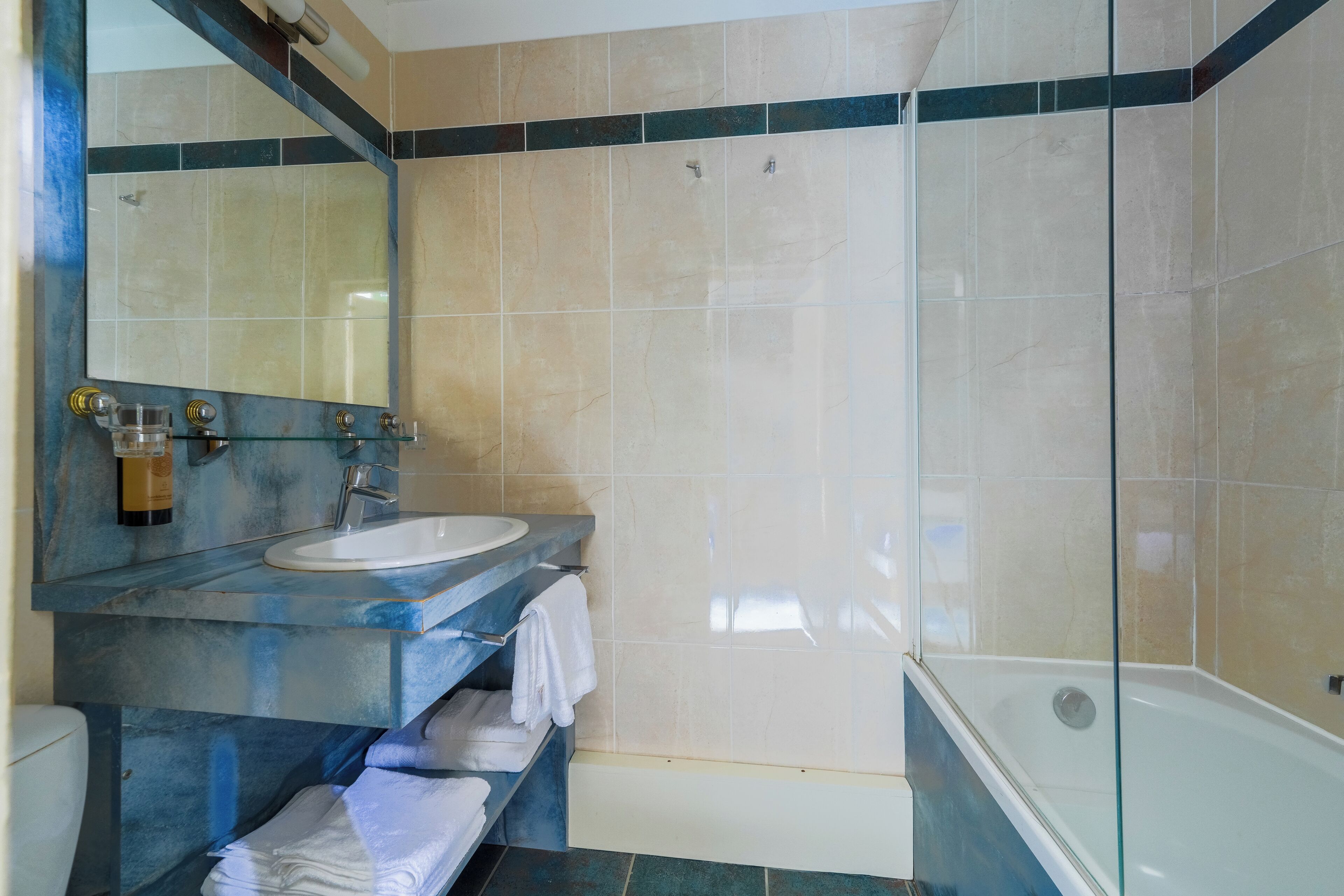 A bathroom with a glass-enclosed shower, a sink with a mirror, and a shelf with towels.