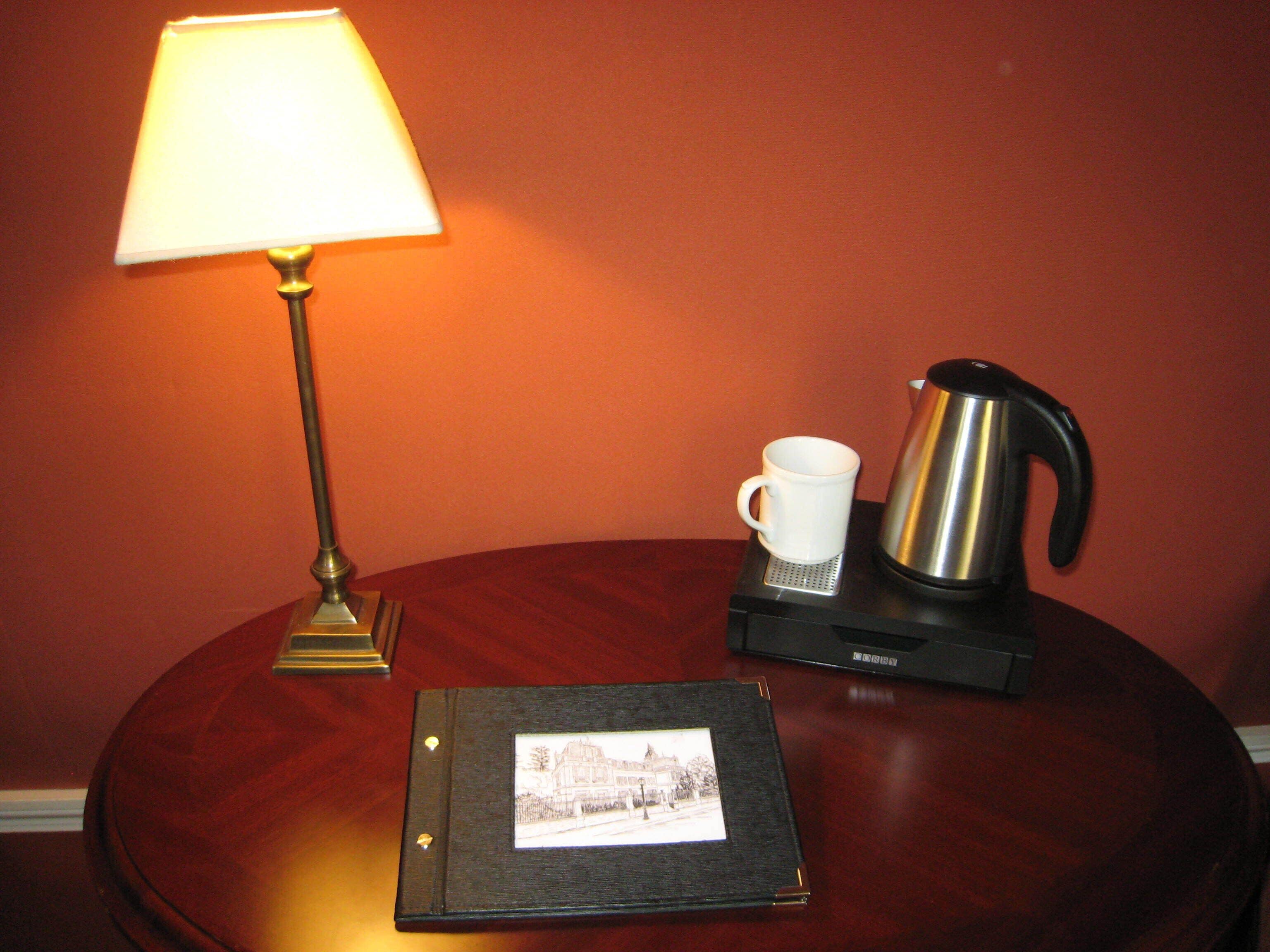 Una mesa de madera con un cuadro enmarcado, una taza blanca, una tetera y una lámpara.