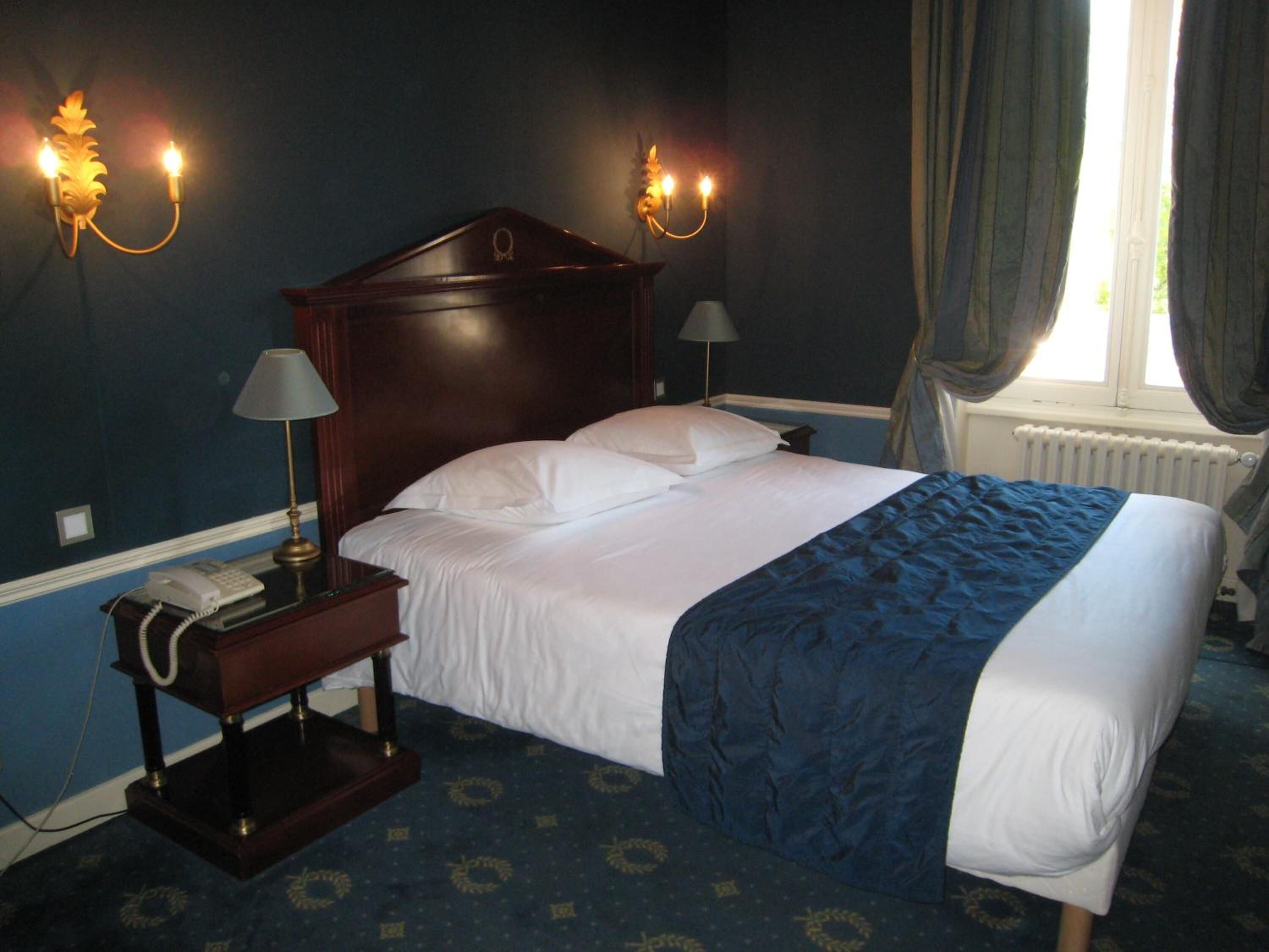 Habitación de hotel con una cama grande, dos lámparas de noche, un teléfono y una ventana con cortinas.