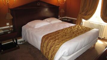 Une chambre d’hôtel avec un grand lit, une tête de lit en bois, deux tables de chevet avec des lampes et une fenêtre avec des rideaux.