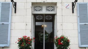 Entrada de un edificio con puertas dobles, dos macetas con plantas de flores rojas y un cartel sobre la puerta.