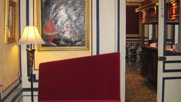 Une pièce avec un fauteuil à revêtement rouge, une table avec des journaux, un tableau encadré et un tapis à motifs.