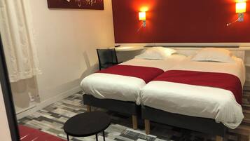 A hotel room with a bed, two bedside tables, a chair, a small table, and a painting on the wall.