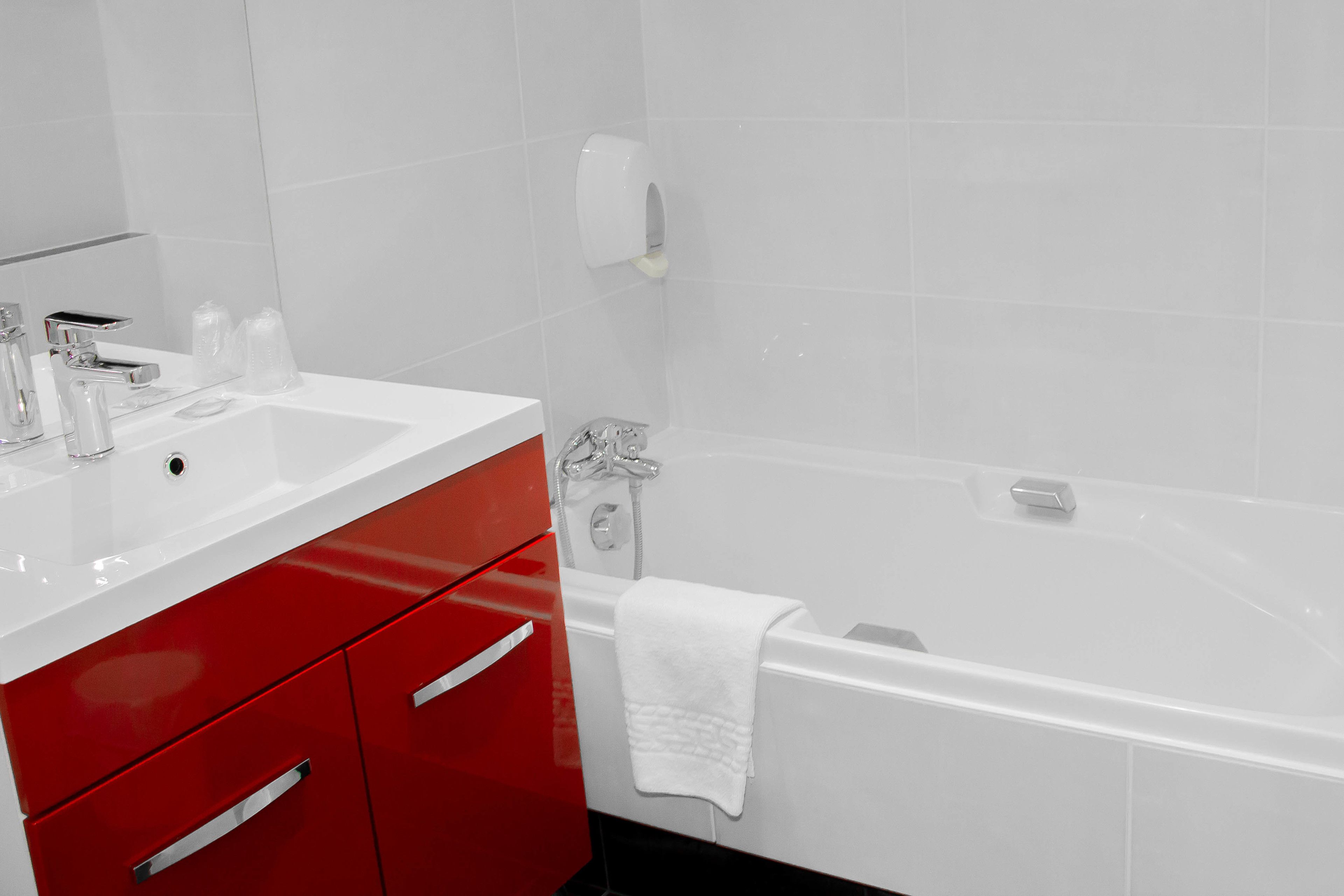 A modern bathroom with a white sink, red vanity, and a white bathtub.