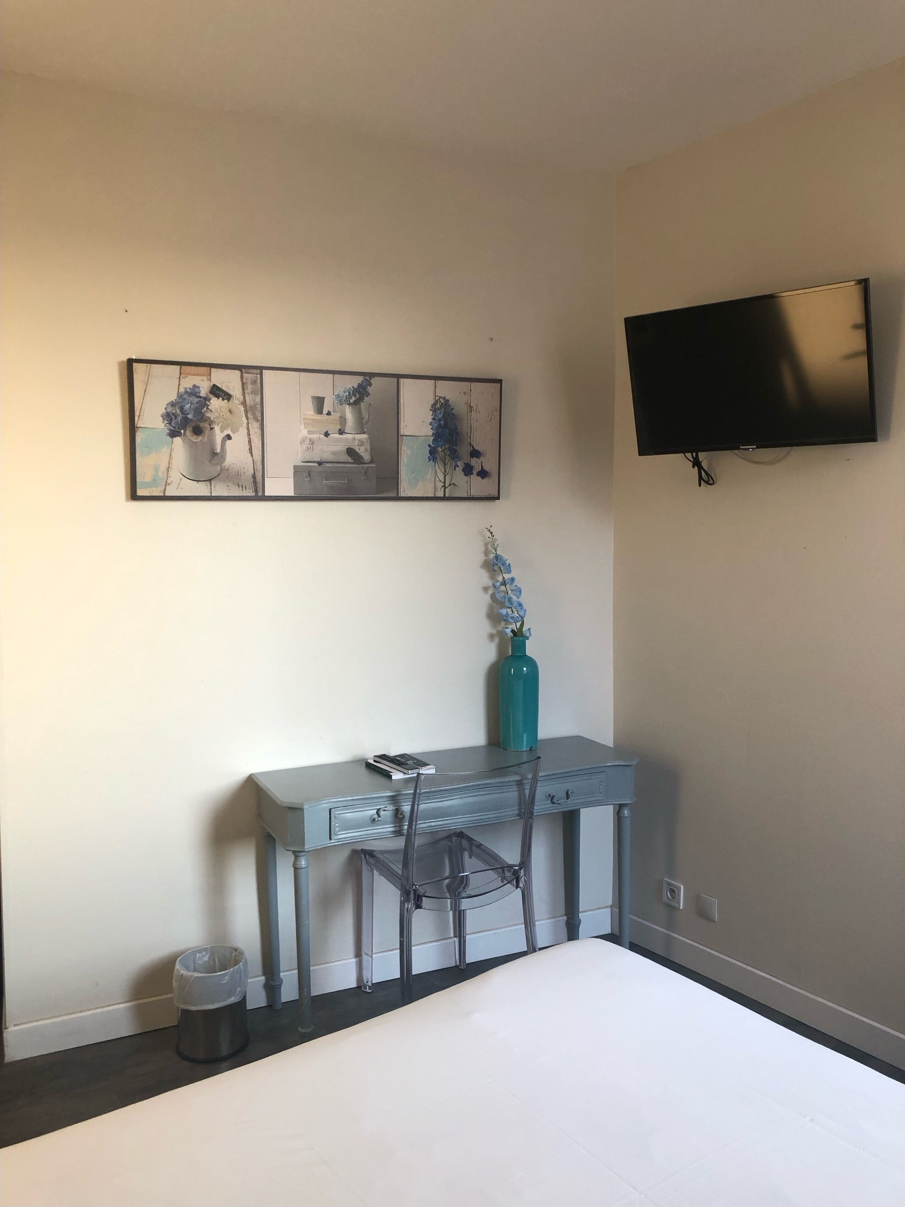 Un dormitorio con una cama, un escritorio con una silla, un televisor y obras de arte en la pared.