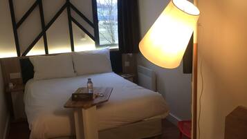 A hotel room with a bed, bedside table, lamp, and a view of the outdoors.