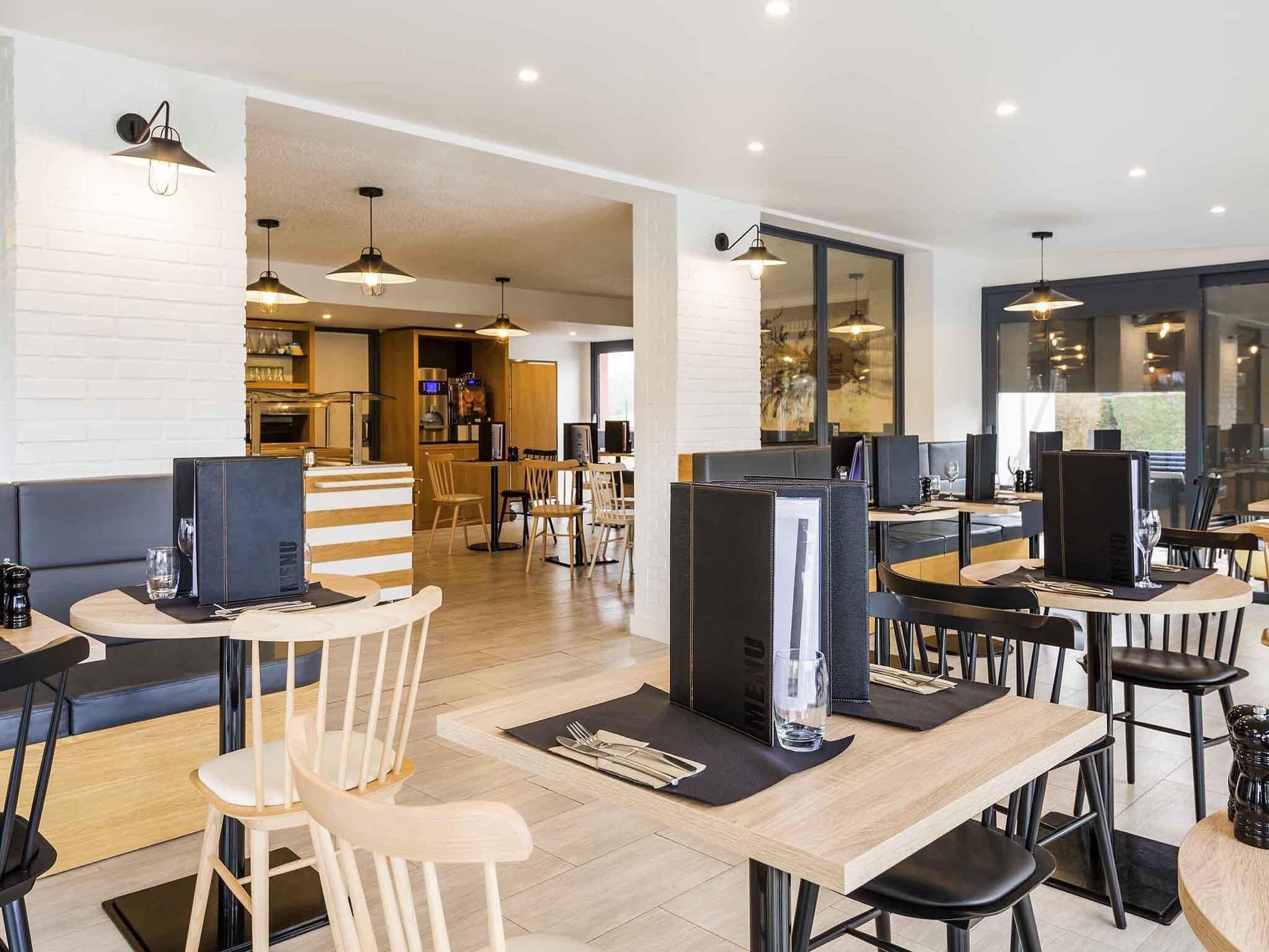 Un restaurant moderne avec des tables en bois, des chaises noires et des luminaires suspendus.