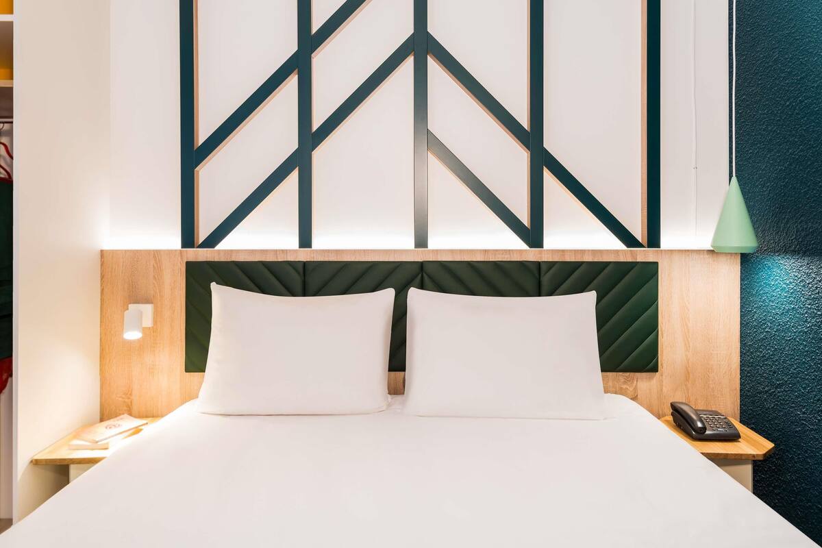 A hotel room with a bed, a bedside telephone, and a wall with geometric patterns.