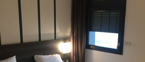 Habitación de hotel con dos camas, una mesita de noche de madera, un control remoto y una botella de agua.