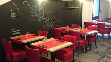 Een restaurant met rode stoelen en tafels, een zwarte muur met een kaart, en verlichting aan het plafond.
