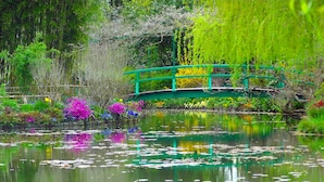 A tranquil garden with a green bridge over a pond, surrounded by lush vegetation and colorful flowers.
