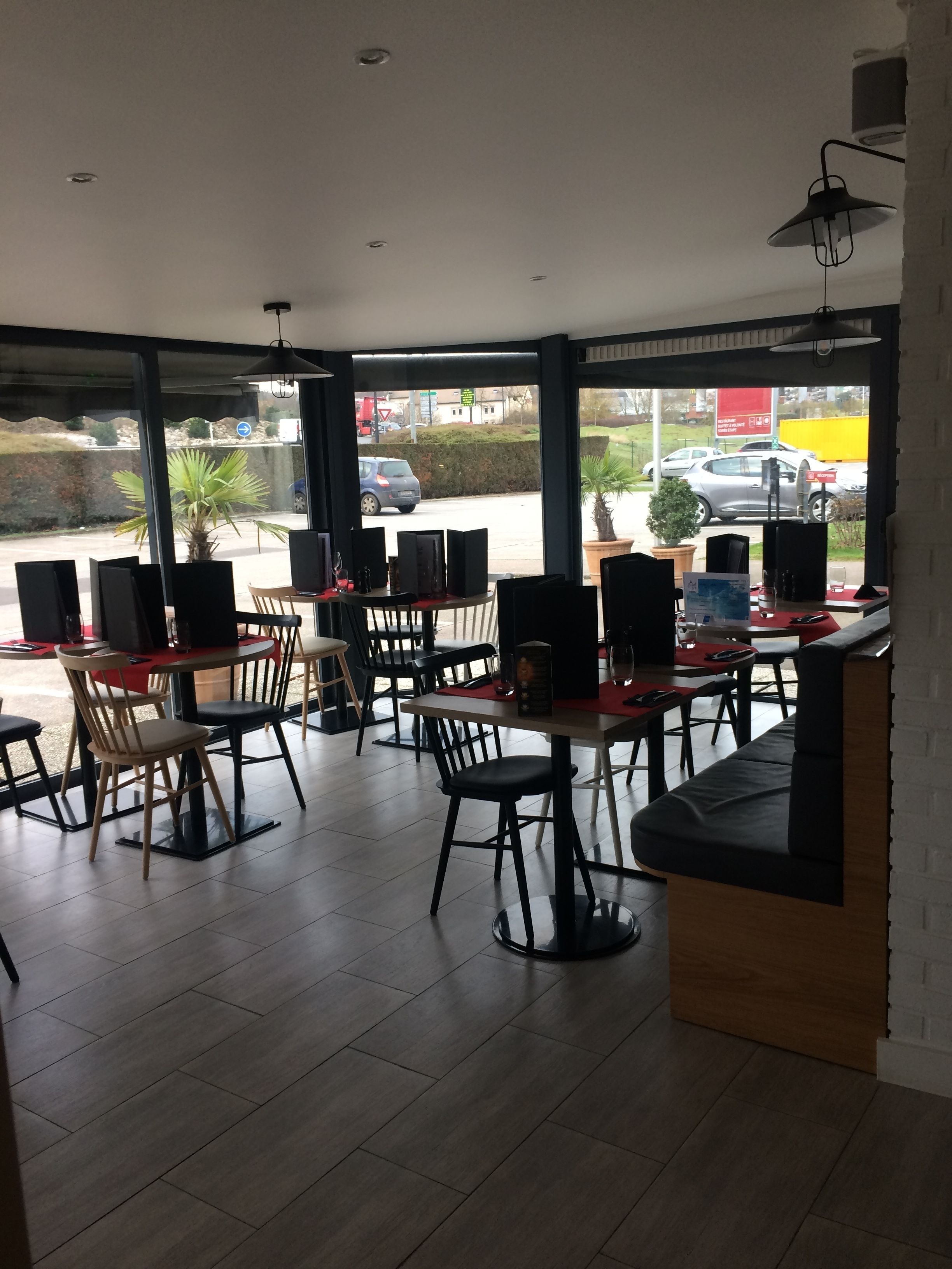 Un restaurant avec des tables et des chaises, de grandes fenêtres et une vue sur la rue.