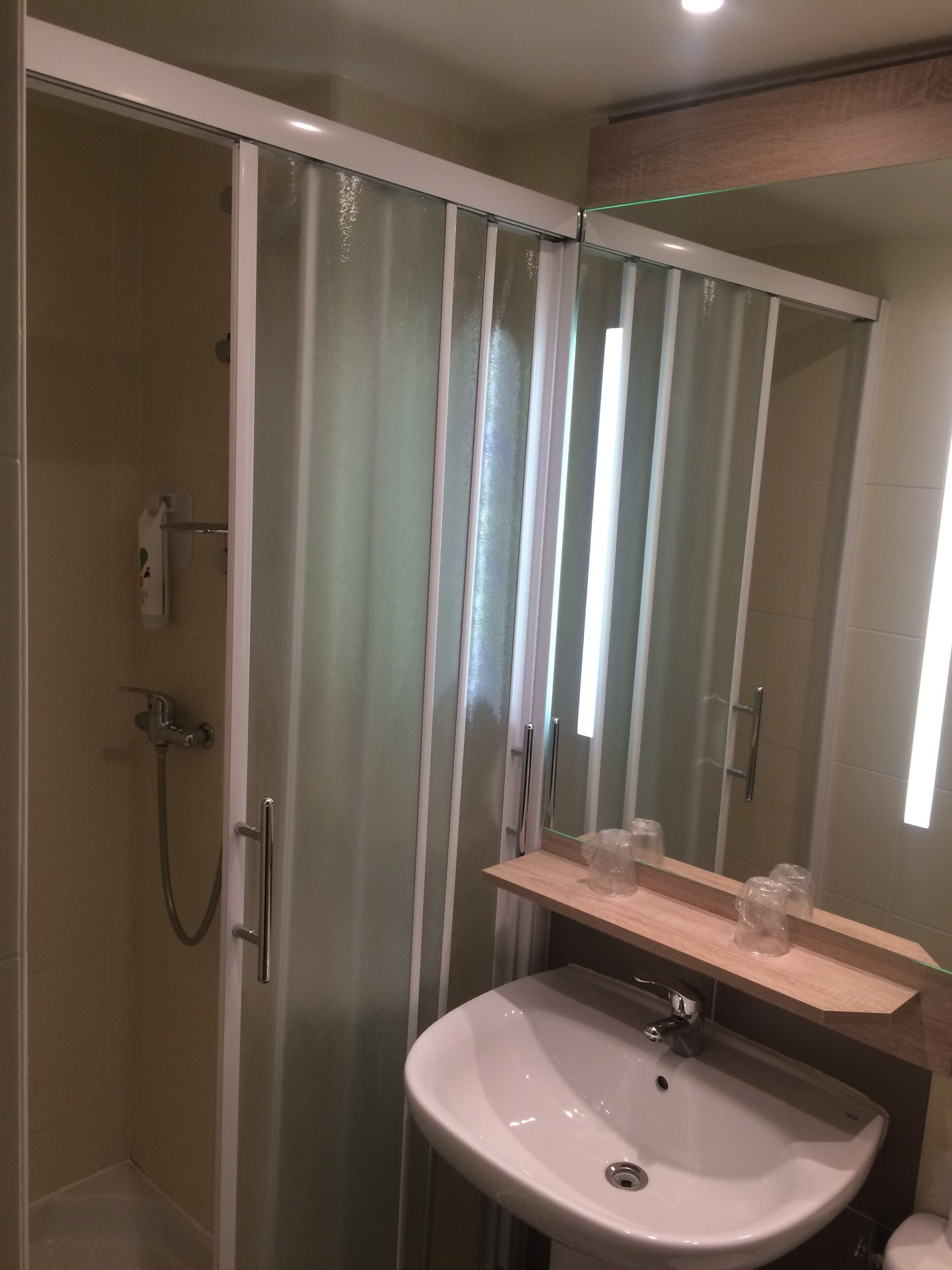 Un baño con cabina de ducha de vidrio, un lavabo blanco y un espejo encima.