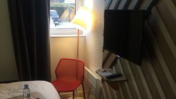 Habitación de hotel con cama, una mesita con un control remoto, una silla roja, una lámpara y un televisor montado en la pared.